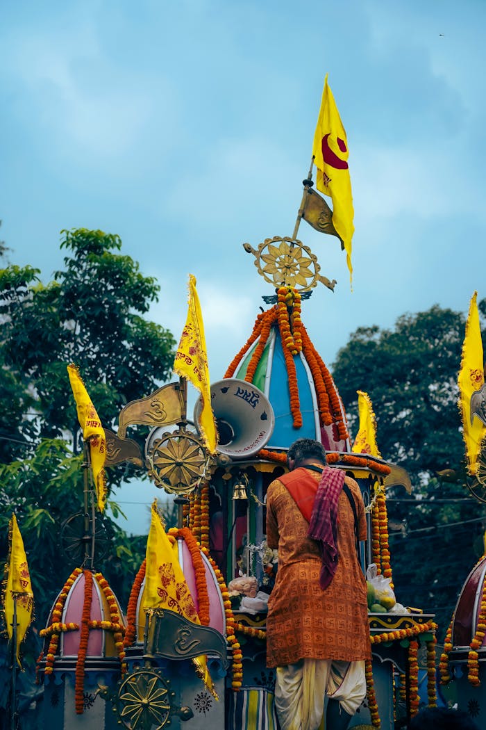 Vibrant Indian procession with decorated chariot and devotee under a cloudy sky.