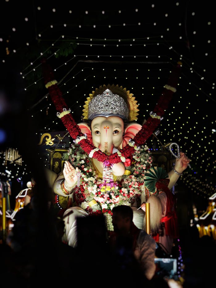 Illuminated Ganesh idol adorned with flowers during a vibrant nighttime festival celebration.