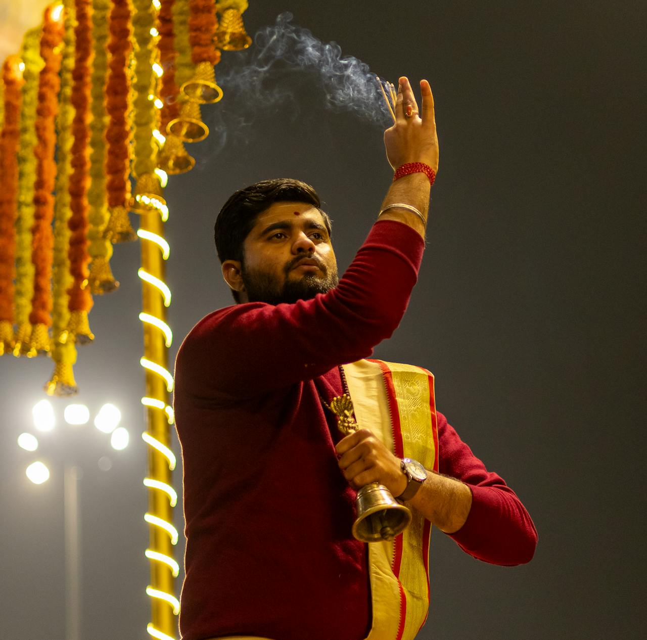 Hindu priest in traditional attire performing a religious ritual with incense at night.