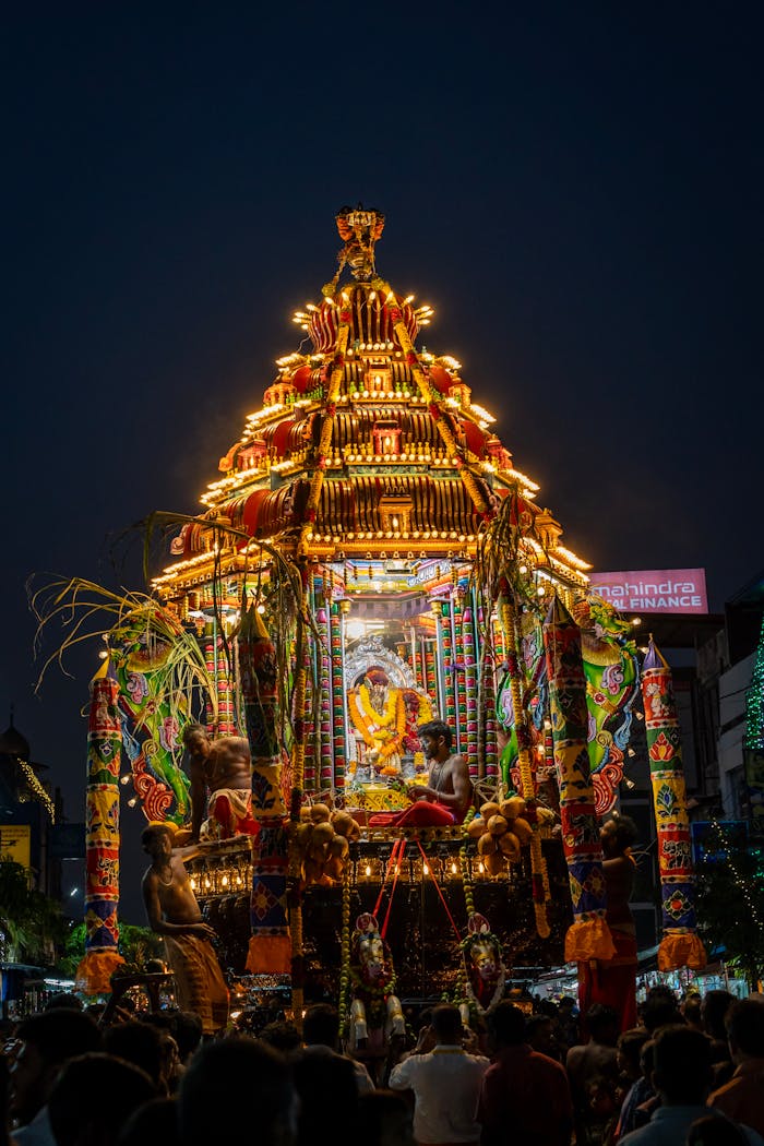 Vibrant illuminated procession with decorated temple chariot in India's night festival under dark sky.