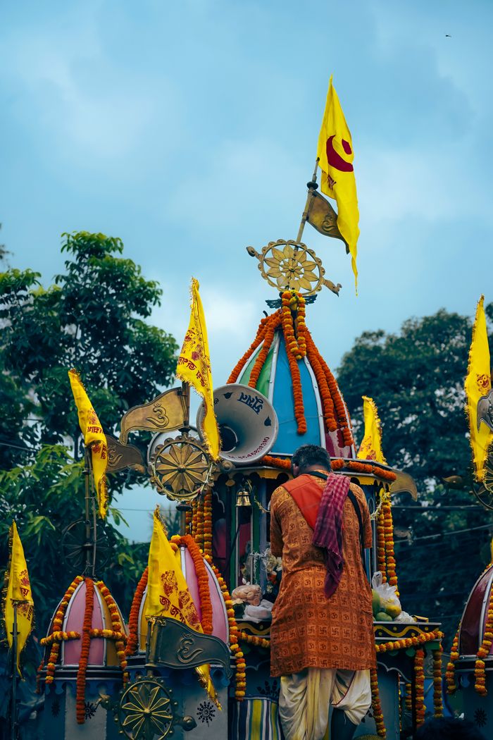 Vibrant Indian procession with decorated chariot and devotee under a cloudy sky.