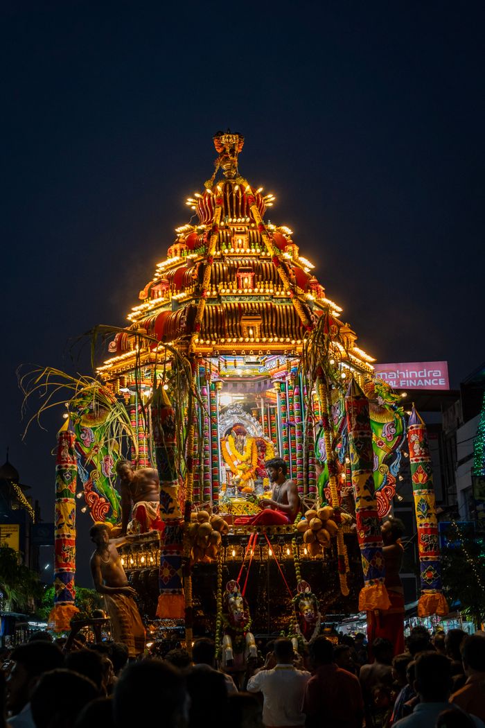 Vibrant illuminated procession with decorated temple chariot in India's night festival under dark sky.